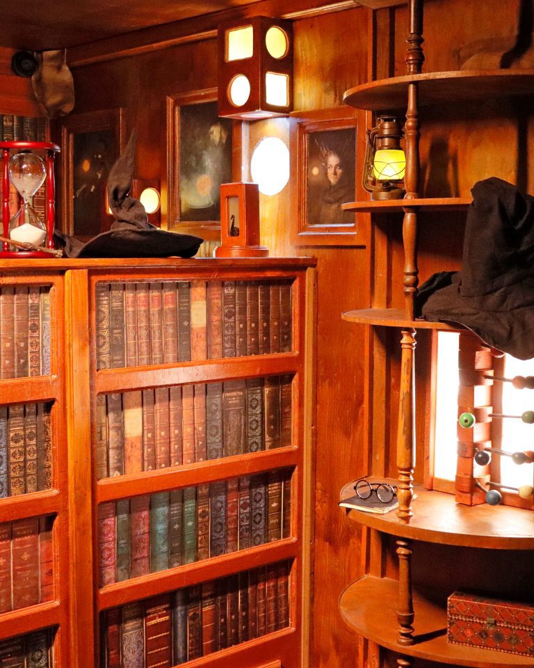 Ein hölzernes Bücherregal, darauf ein Zauberhut, eine Sanduhr, ein Zauberstab und Zaubertränke.