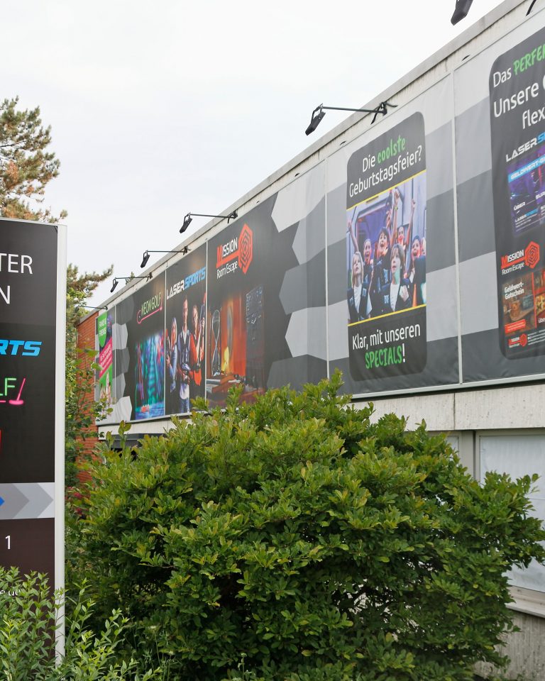 Ein Pylon mit einem Pfeil zum Eingang von funXperience Göttingen und eine Hauswand mit einem großen Banner zu den Erlebnissen