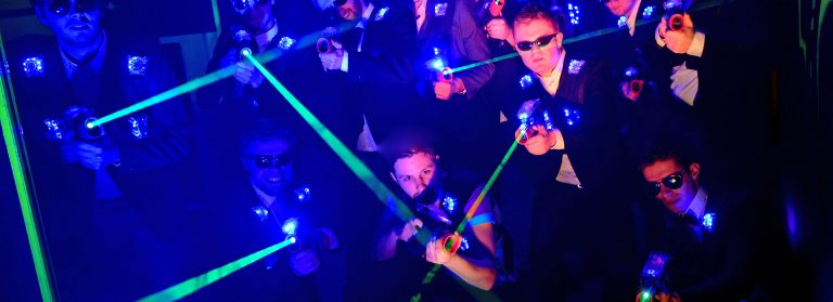 Eine Gruppe von Männern in Anzügen mit Lasertag-Phasern in einem dunklen Raum.