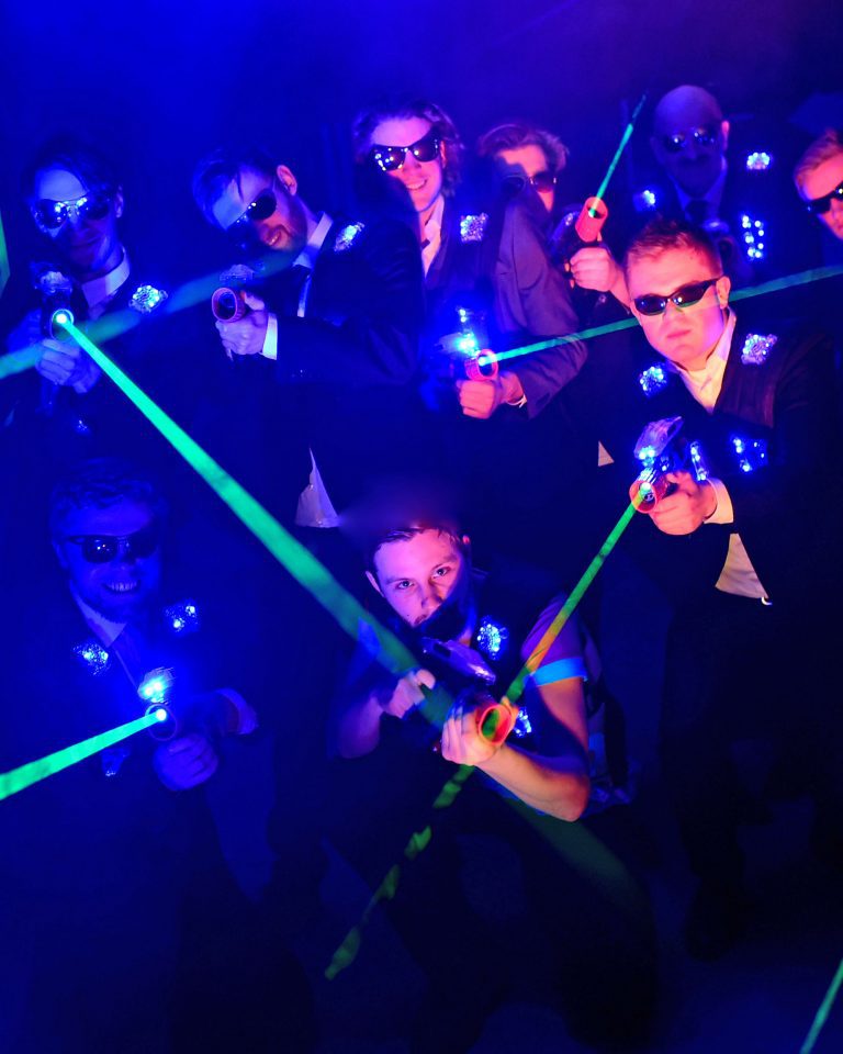 Eine Gruppe von Männern in Anzügen mit Lasertag-Phasern in einem dunklen Raum.