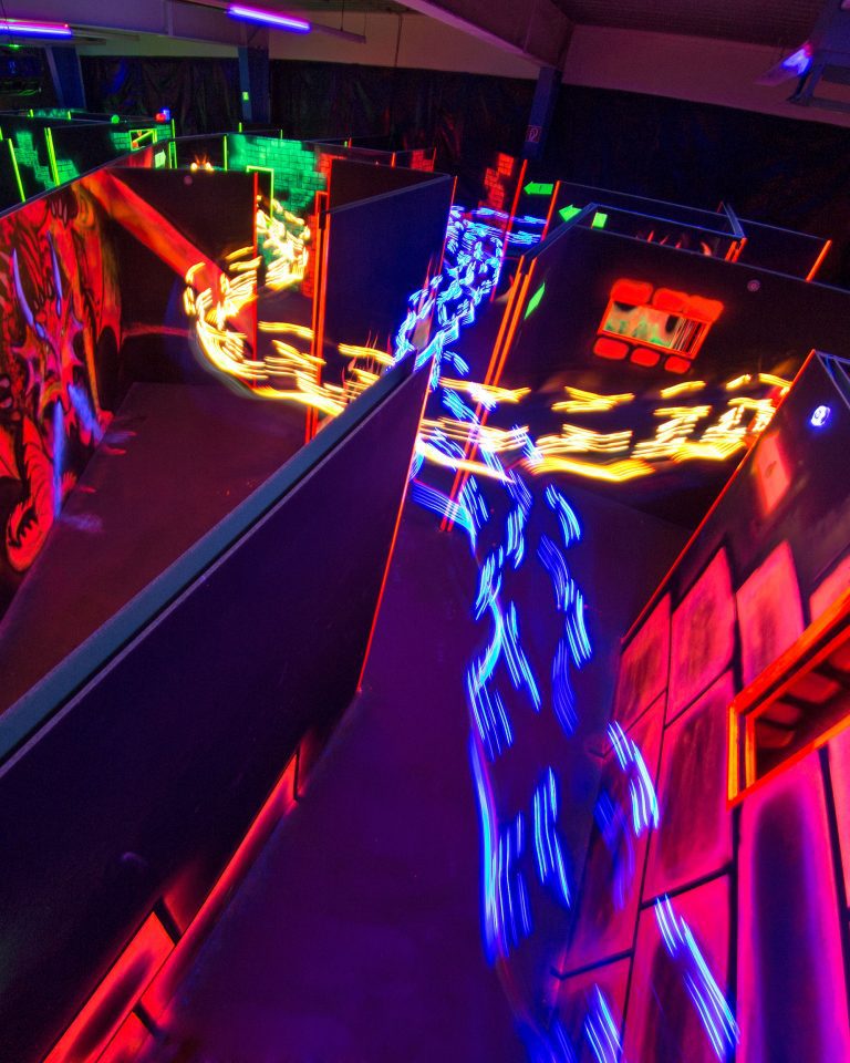 Eine bunte Lasertag-Arena mit Schlieren von Lasertag-Spielern. An einer Wand ein Drache.