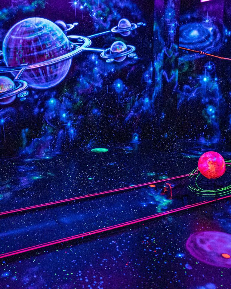 Eine Minigolfbahn im Weltall-Raum von NeonGolf, bei der der Ball durch ein Gitter einmal um einen pinken Planeten und dann ins Loch gespielt wird.
